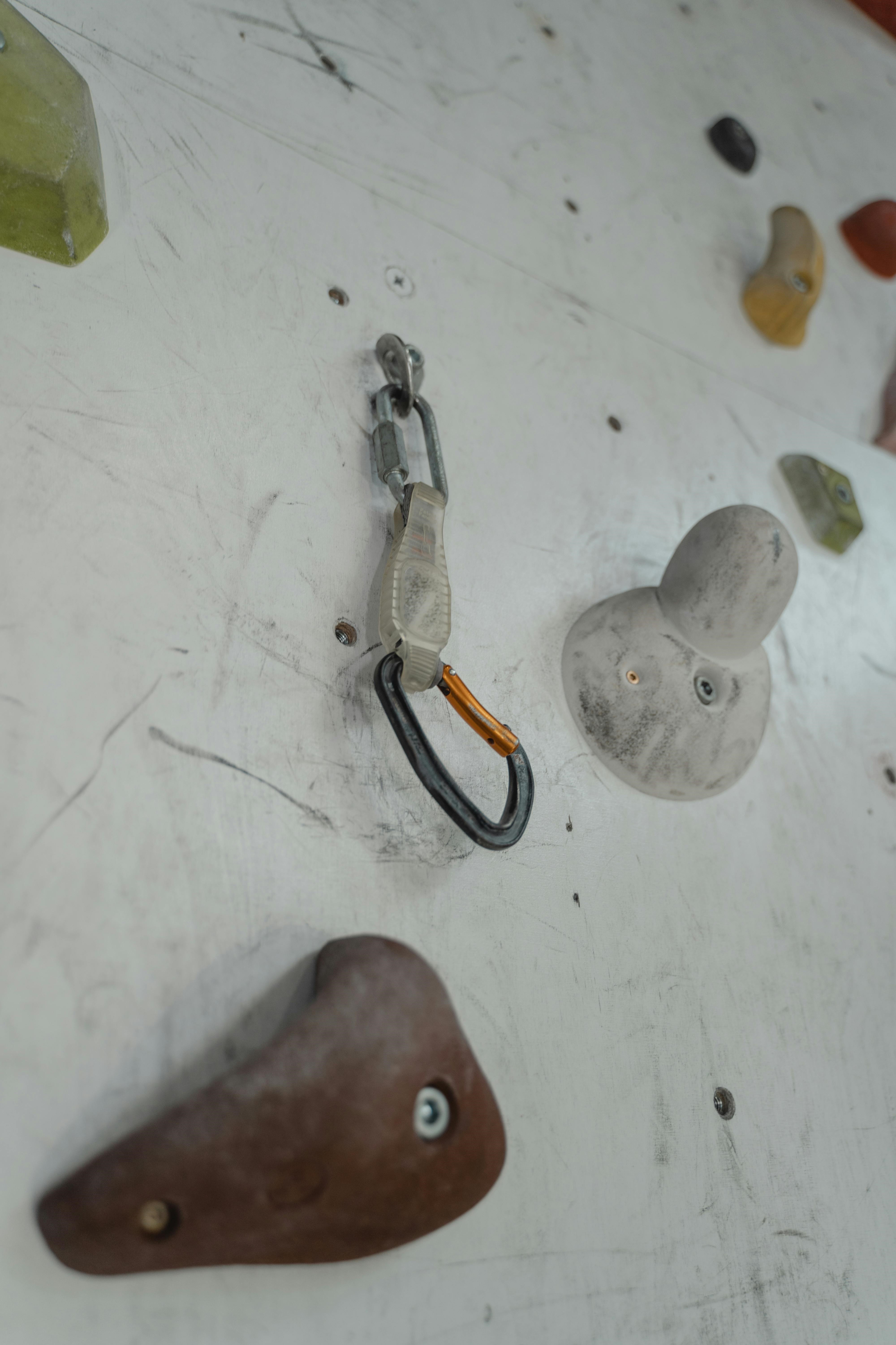 Picture of a carabiner clipped on a climbing wall with an orange anodized finish.